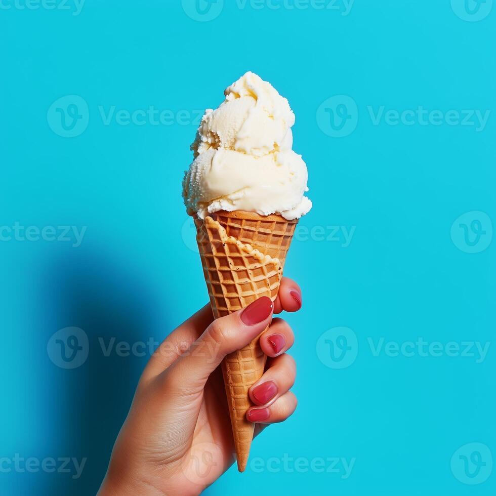 A person holds a delicious ice cream cone topped with creamy vanilla, set against a bright blue background, perfect for a summer treat photo