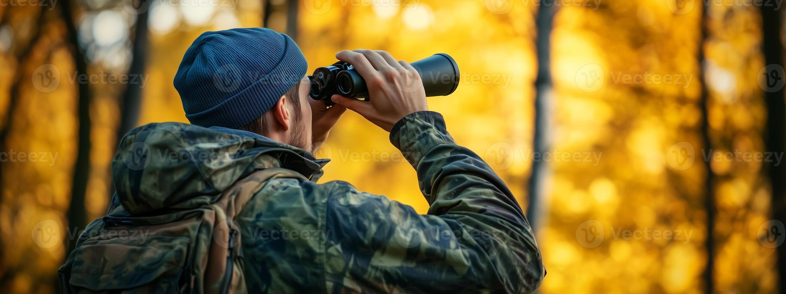 A nature enthusiast observes wildlife through binoculars in a beautiful autumn forest surrounded by vibrant foliage photo