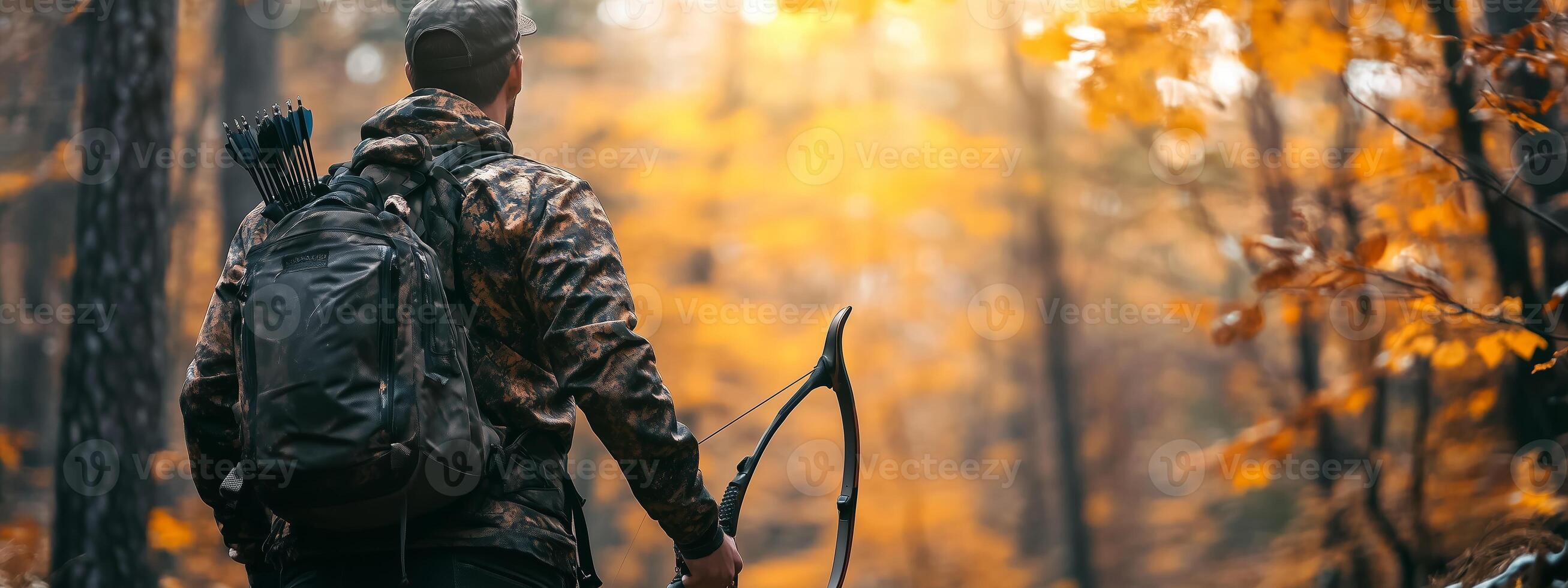 A hunter stands in a colorful forest, preparing for bowhunting in the autumn sunlight among vibrant leaves in a peaceful wilderness photo