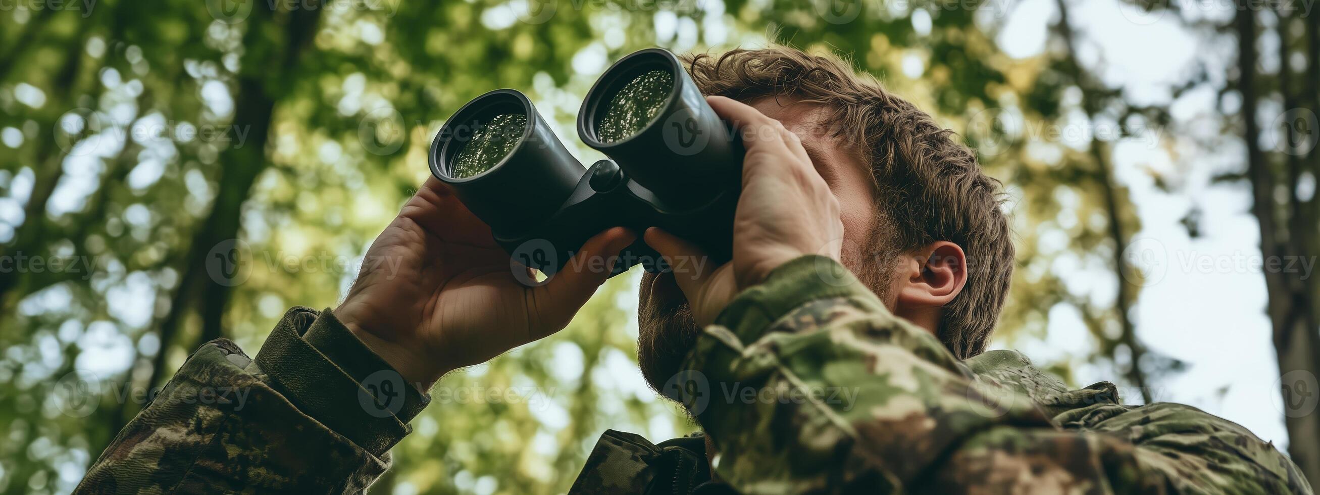 A soldier observes wildlife through binoculars in a dense forest during a daytime expedition in the wilderness photo