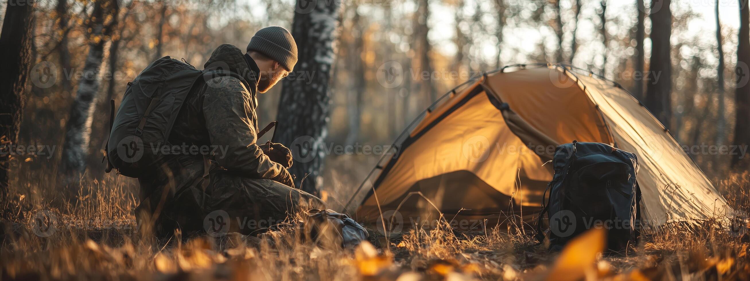 A camper prepares for the evening by his tent in a tranquil forest during golden hour in autumn photo