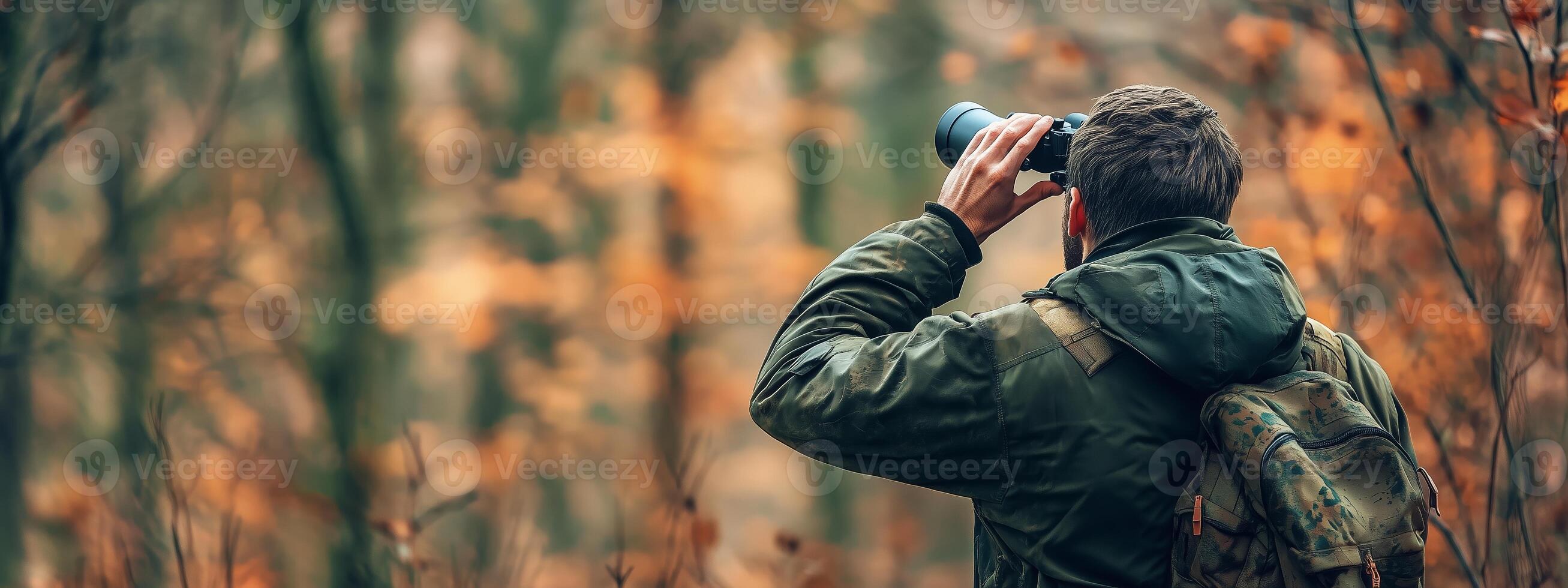 A wildlife enthusiast observes birds through binoculars during autumn in a serene forest setting photo