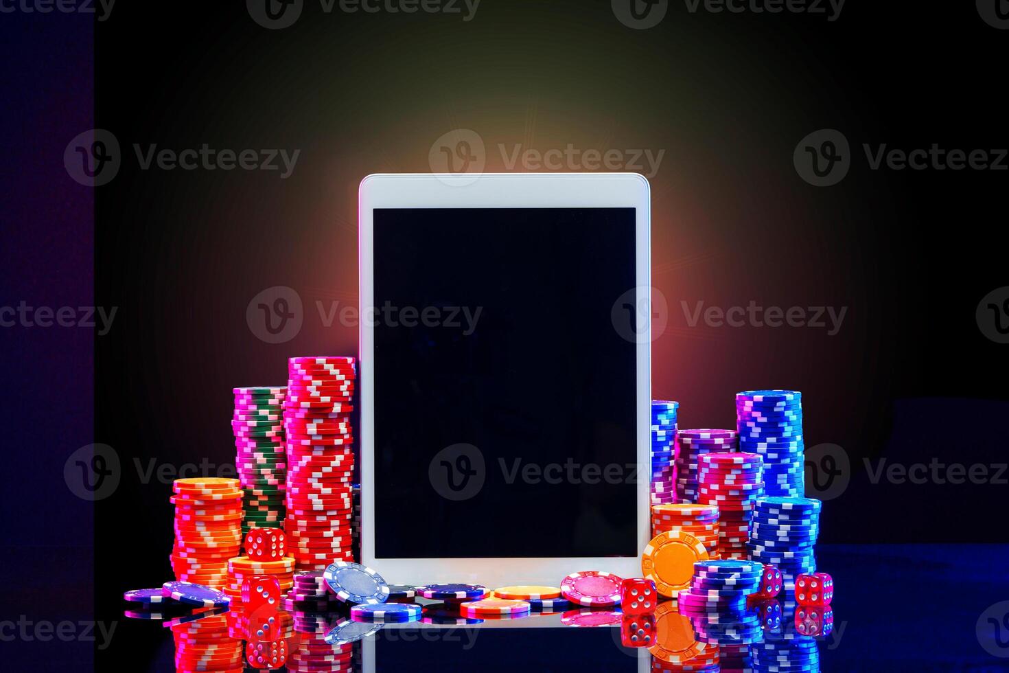 A gaming tablet surrounded by colorful poker chips at a casino table during a night gambling session photo