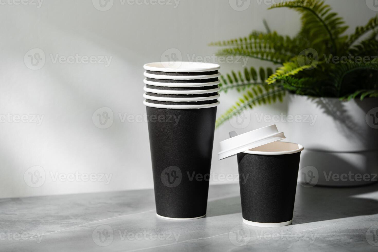 Stack of disposable cups beside a potted plant on a marble surface in natural light photo
