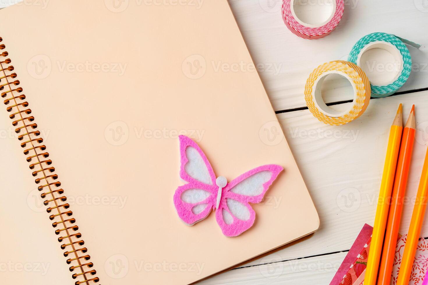 Colorful stationery arrangement with a butterfly sticker on a blank notebook at a wooden table in natural light photo