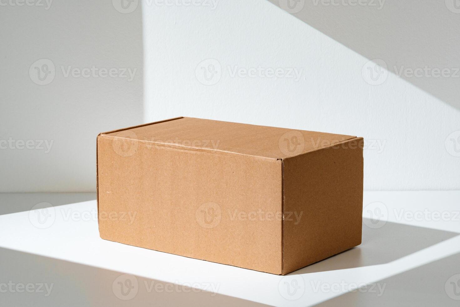 Simple brown cardboard box positioned on a white surface with soft angled shadows in natural light photo