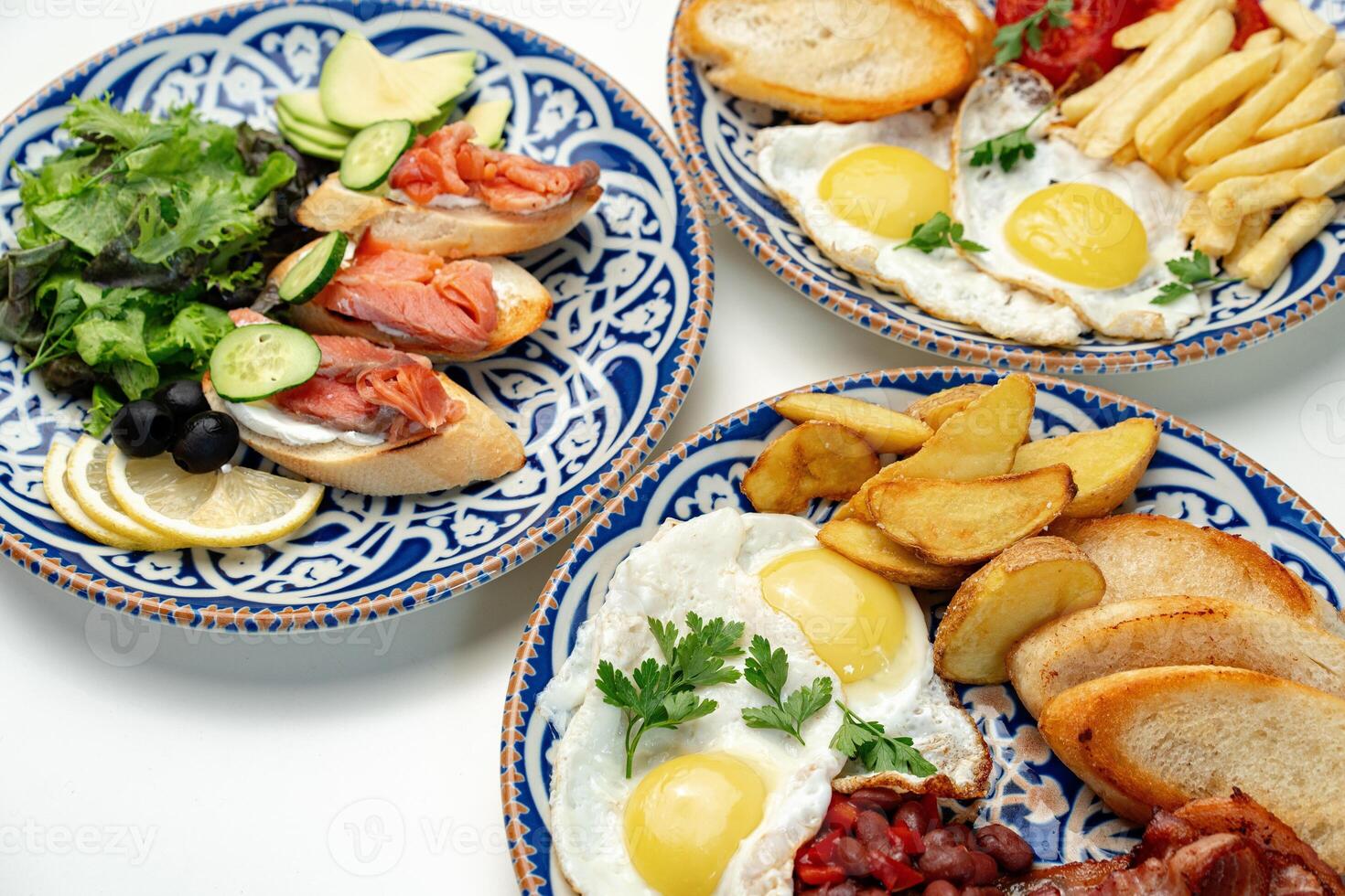 Traditional breakfast plates featuring eggs, sausages, and various accompaniments arranged artistically on a white background photo