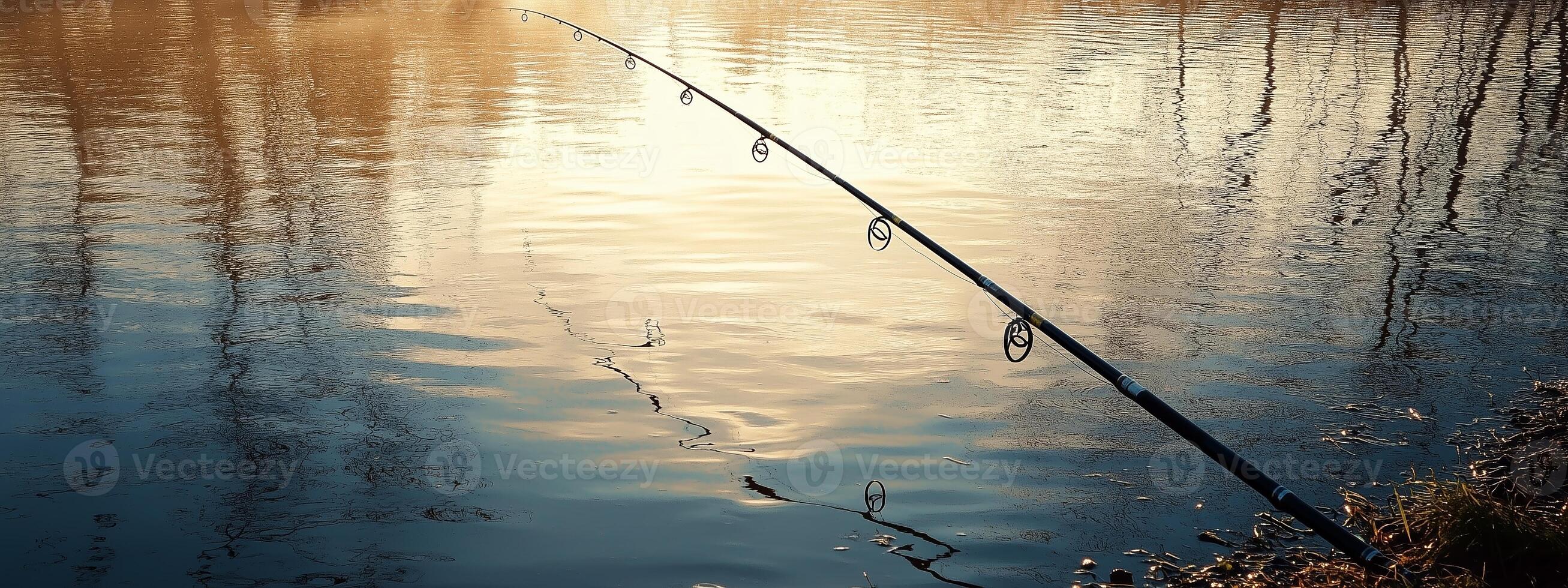 Fishing rod resting by a tranquil lake during sunset, reflecting peaceful scenery with calm waters and surrounding trees photo