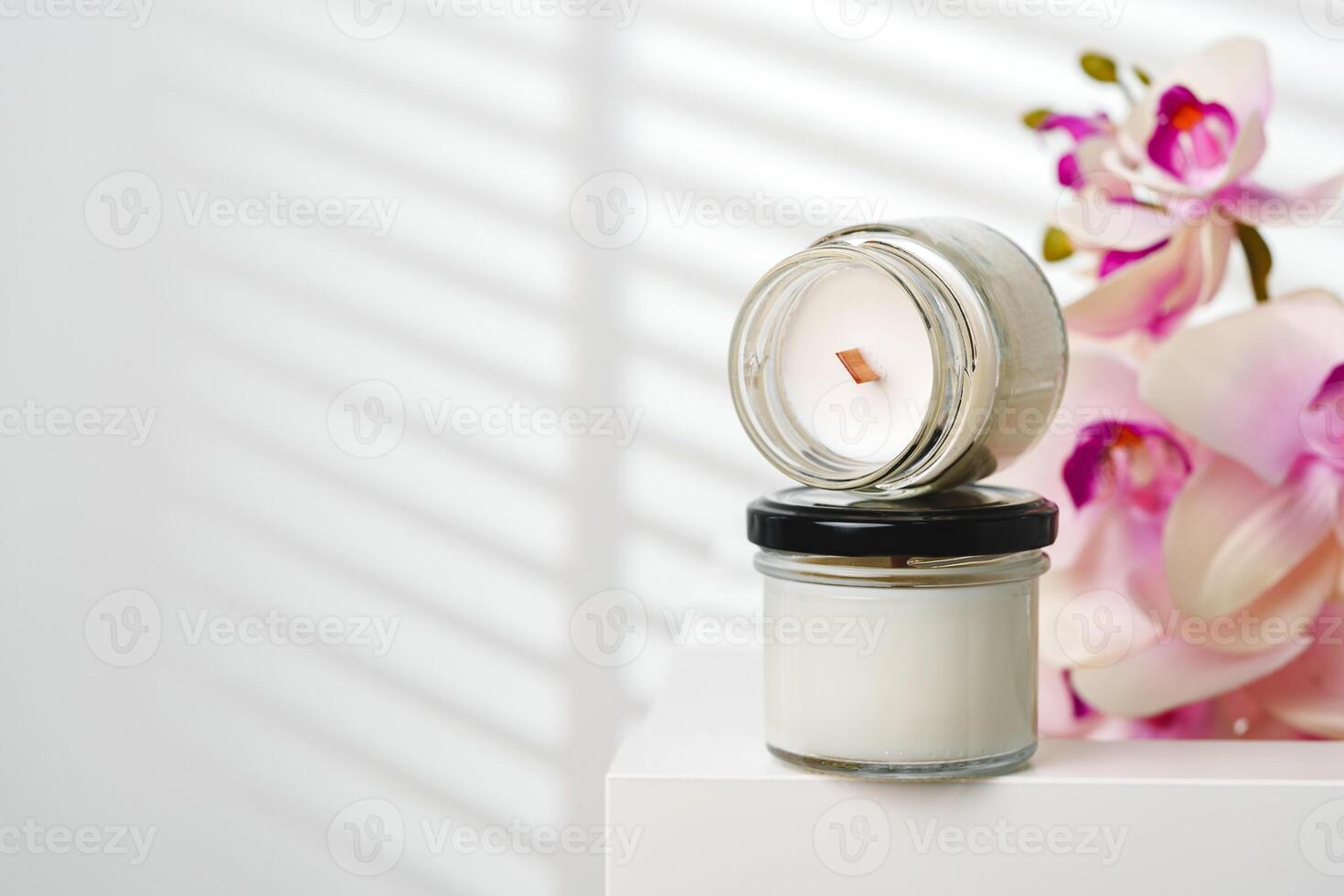 Opened Scented Candle Jar on a White Stand Near a Blurry Orchid Flower photo