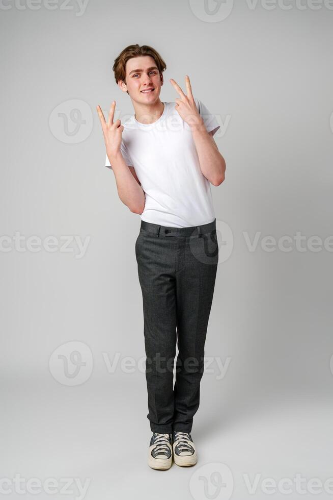 Young Man in White T-Shirt and Gray Pants Making Peace Sign With Both Hands in Studio photo