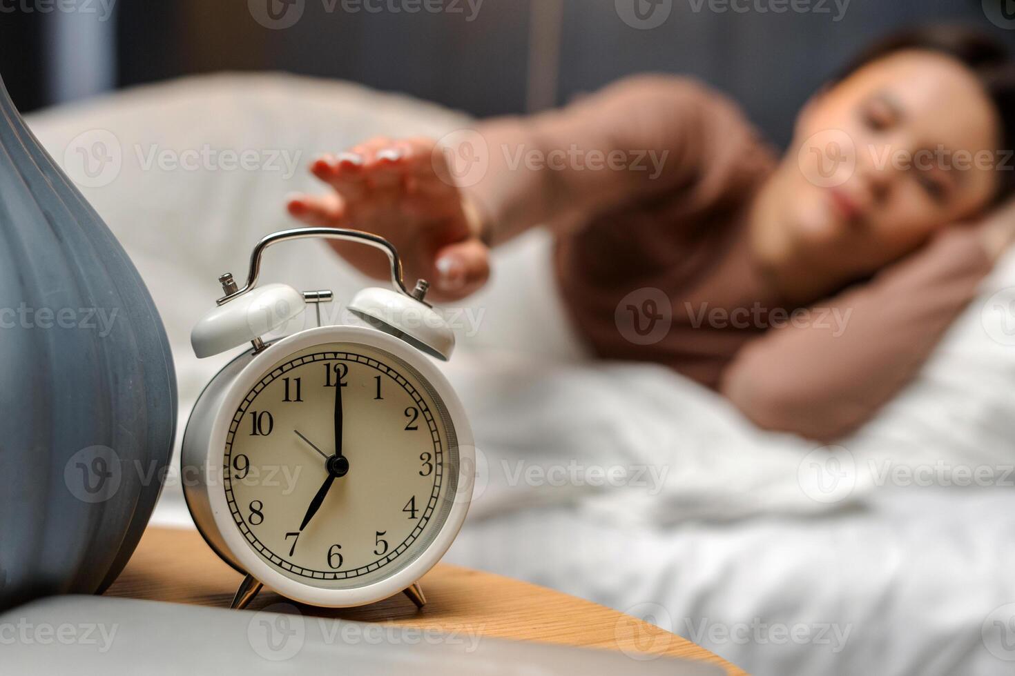 Young female turning off alarm clock on nightstand at 6am photo