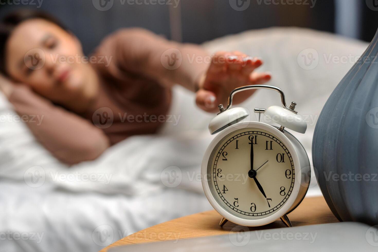Young female turning off alarm clock on nightstand at 6am photo