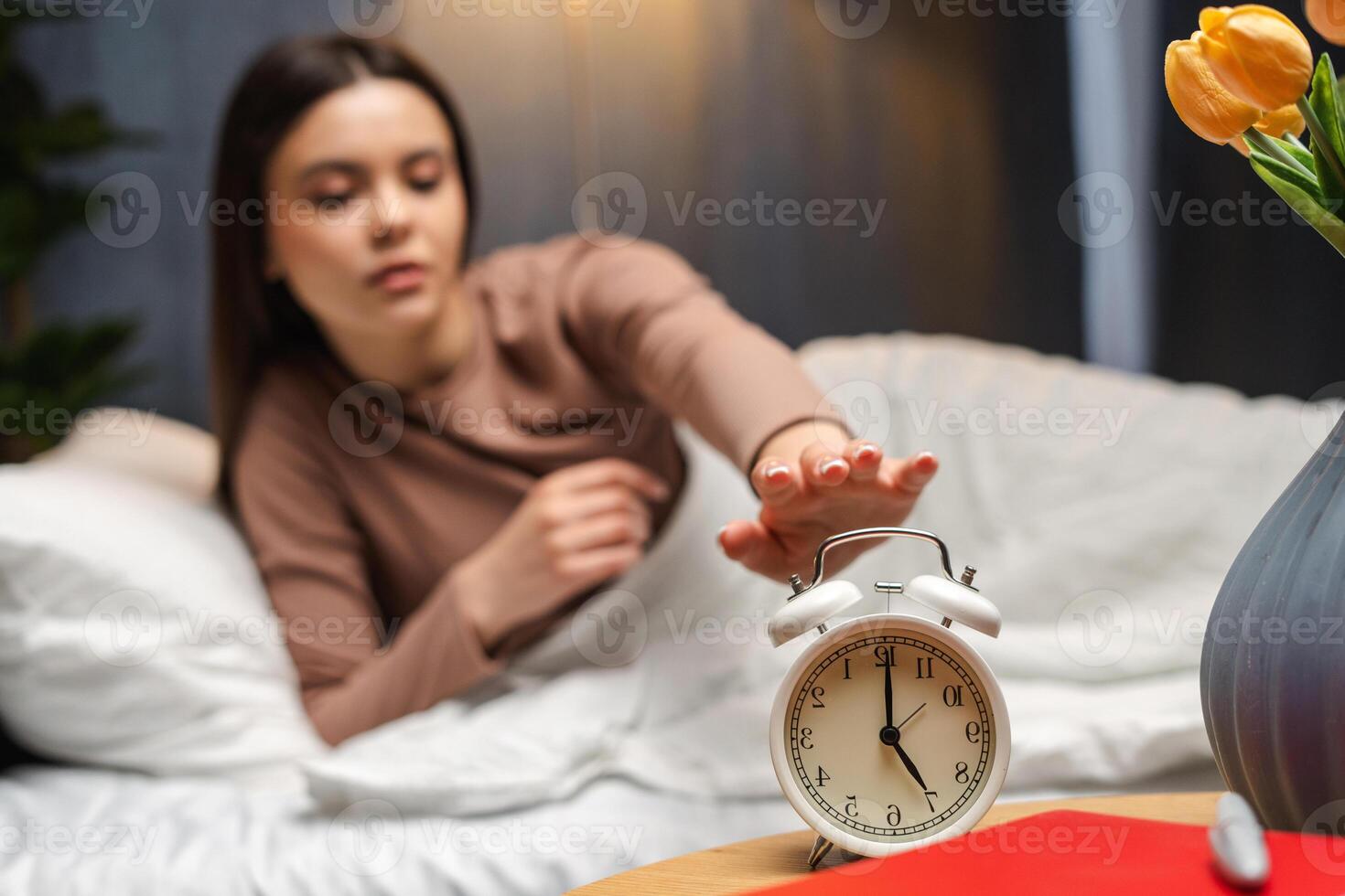 Young girl, teenager turning off alarm clock waking up late photo