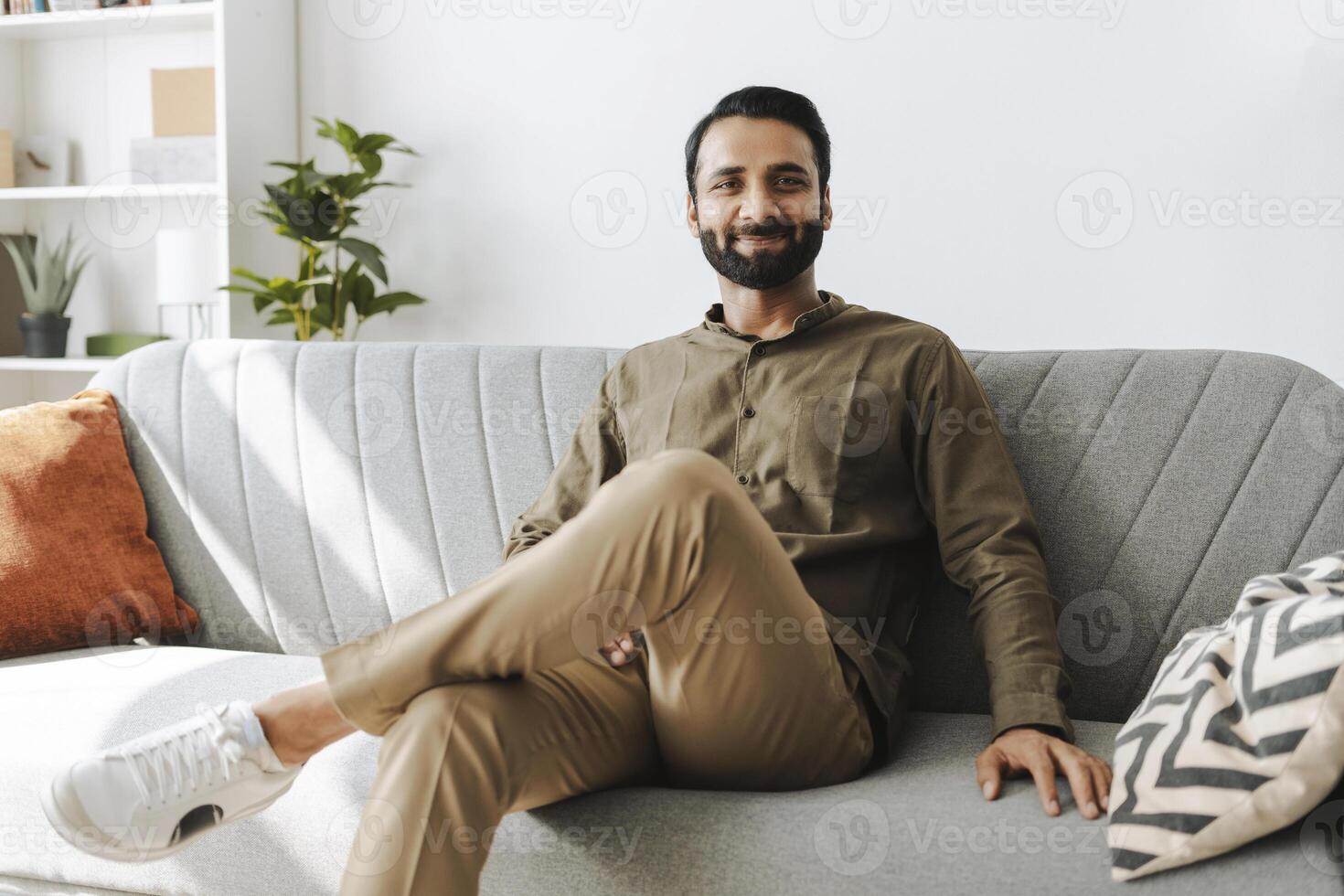 Confident entrepreneur, smiling Indian man sitting on sofa at home, looking at camera photo