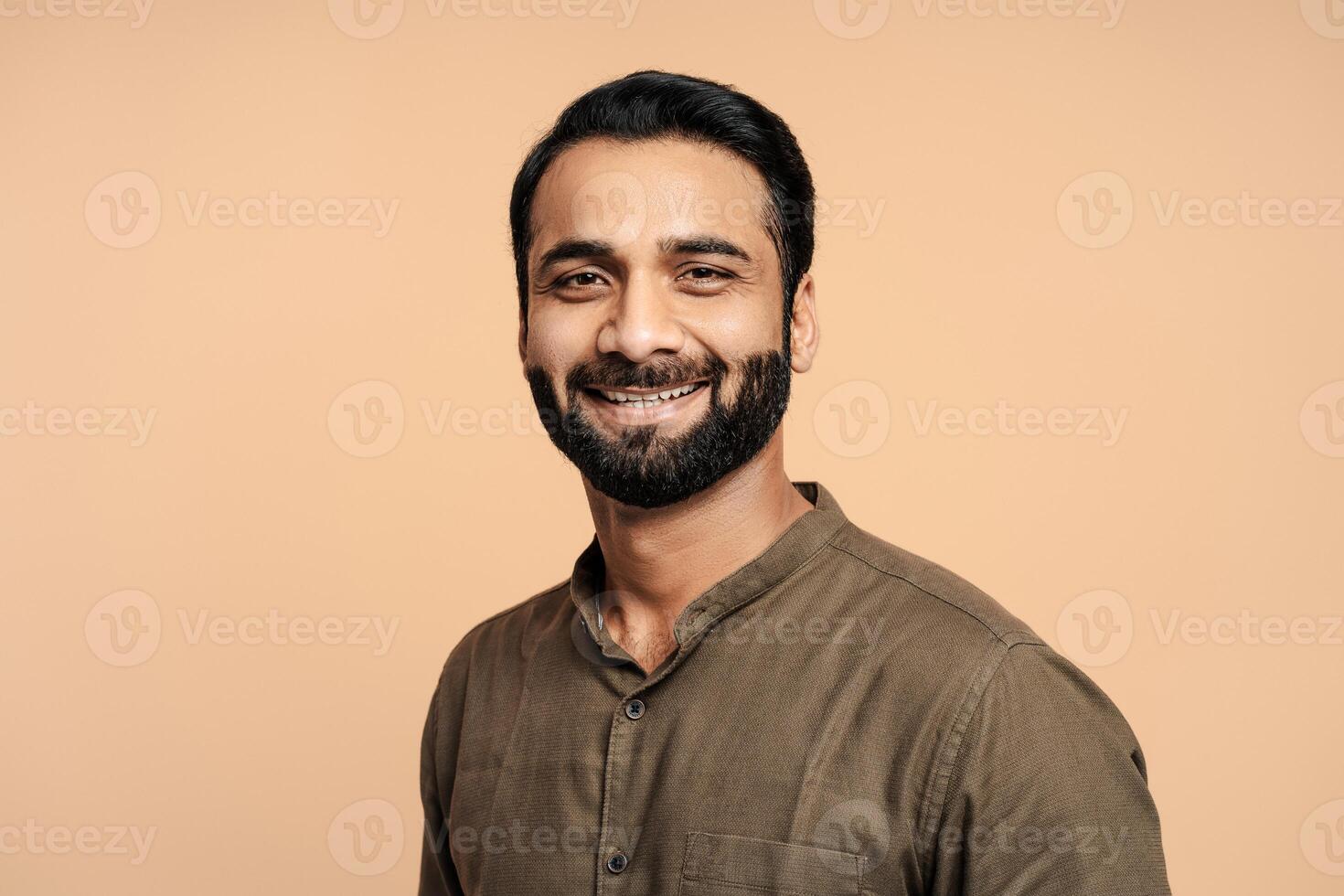 Portrait of positive, handsome indian man smiling and posing isolated on beige background photo