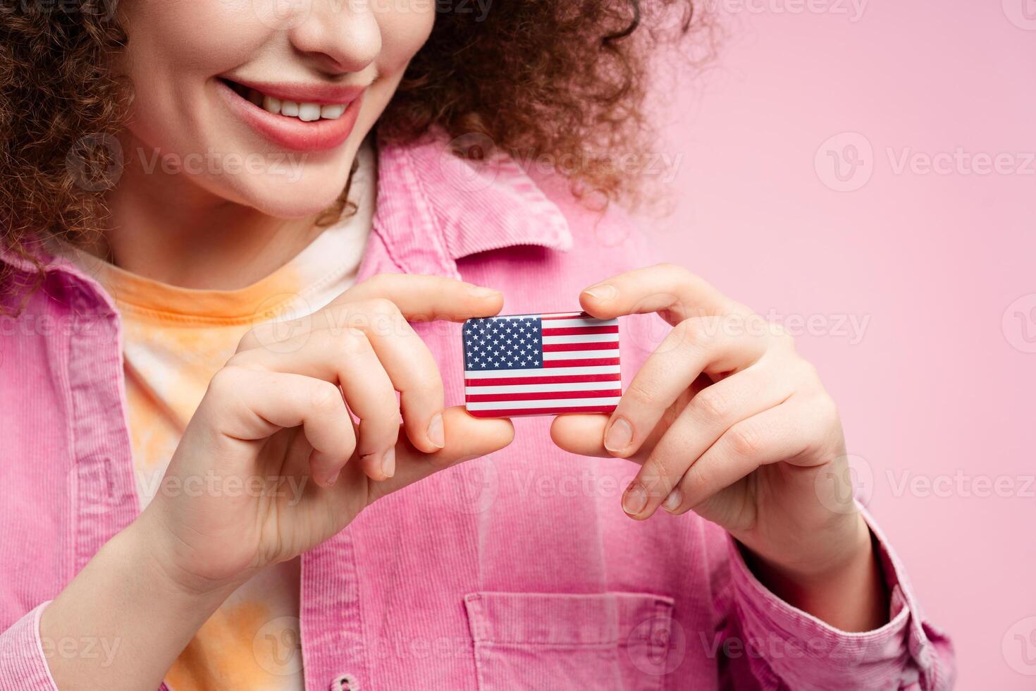 Smiling attractive curly haired woman holding American flag icon, closeup, selective focus on hands photo