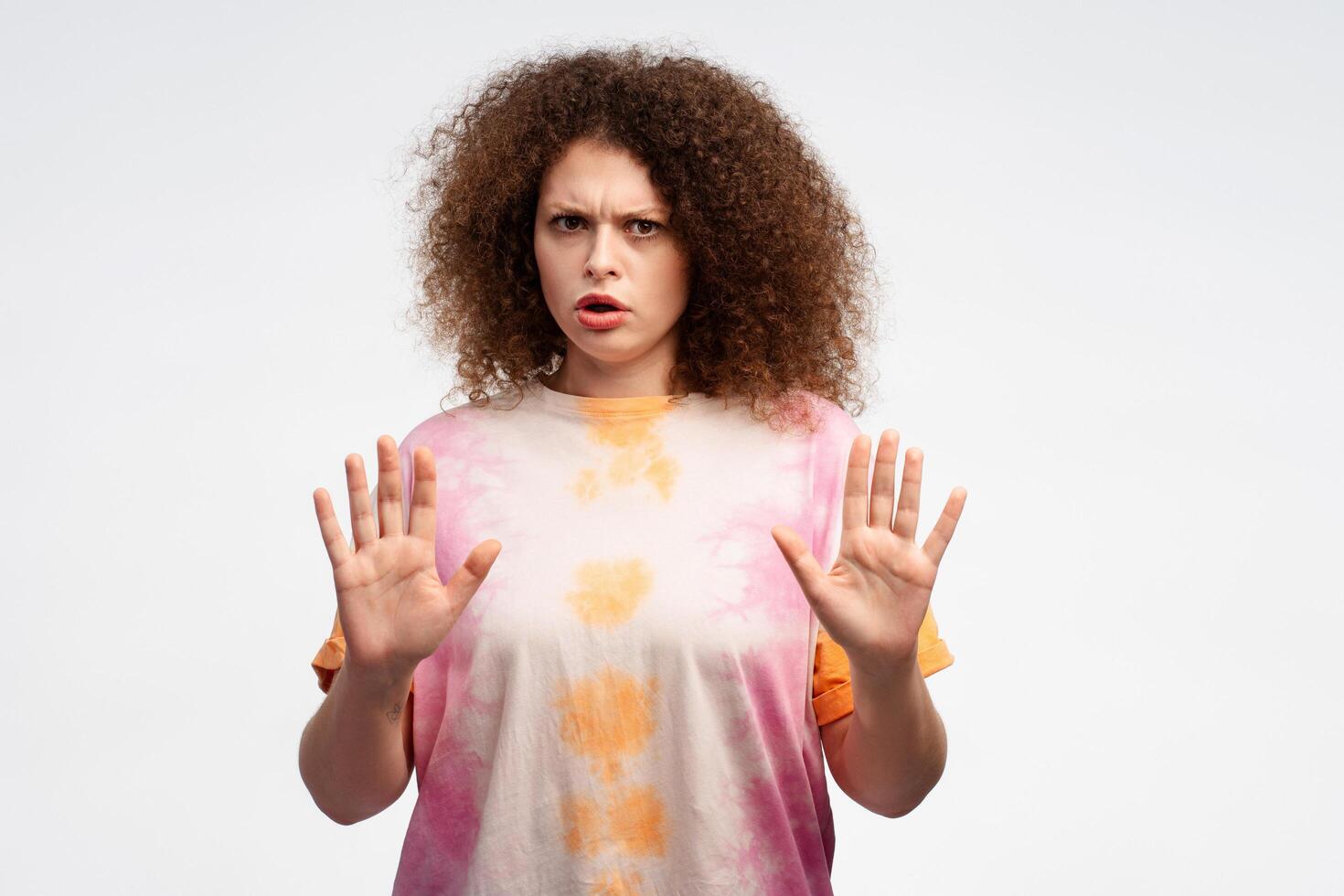 Serious, pensive woman with curly hair wearing summer t shirt showing stop sign, looking at camera photo
