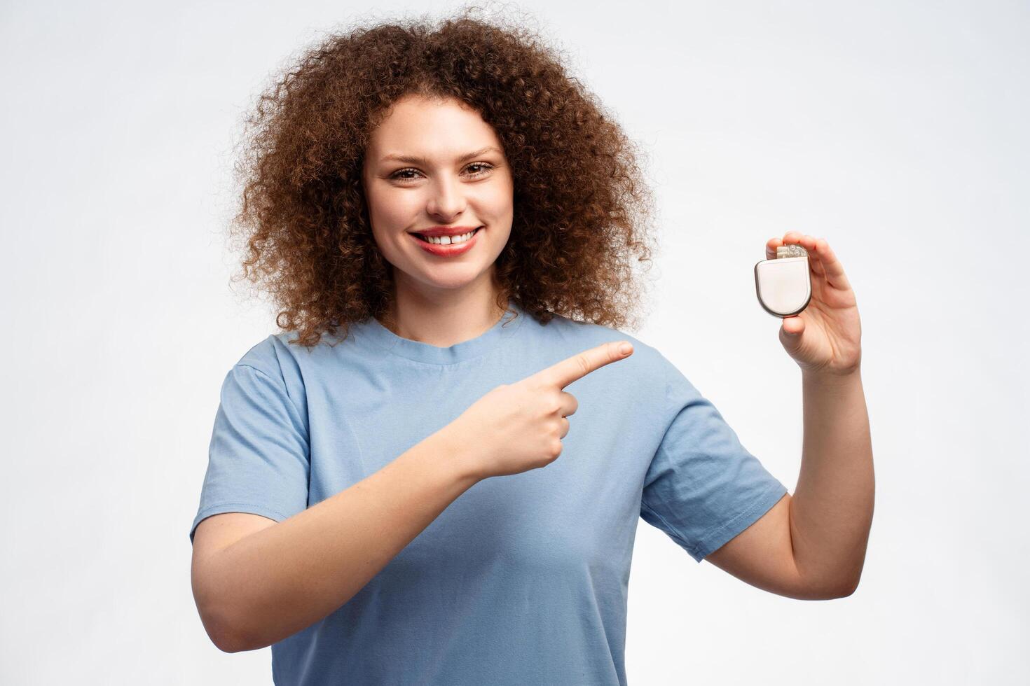 Attractive smiling woman with curly hair holding pacemaker pointing finger at it looking at camera photo