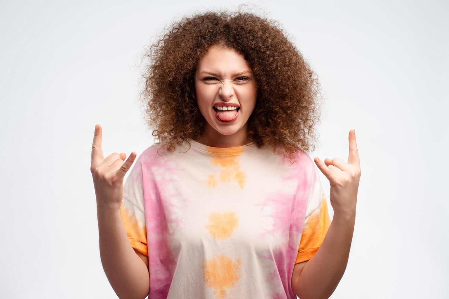 Happy beautiful woman with curly hair wearing summer t shirt showing fingers rock n roll sign photo