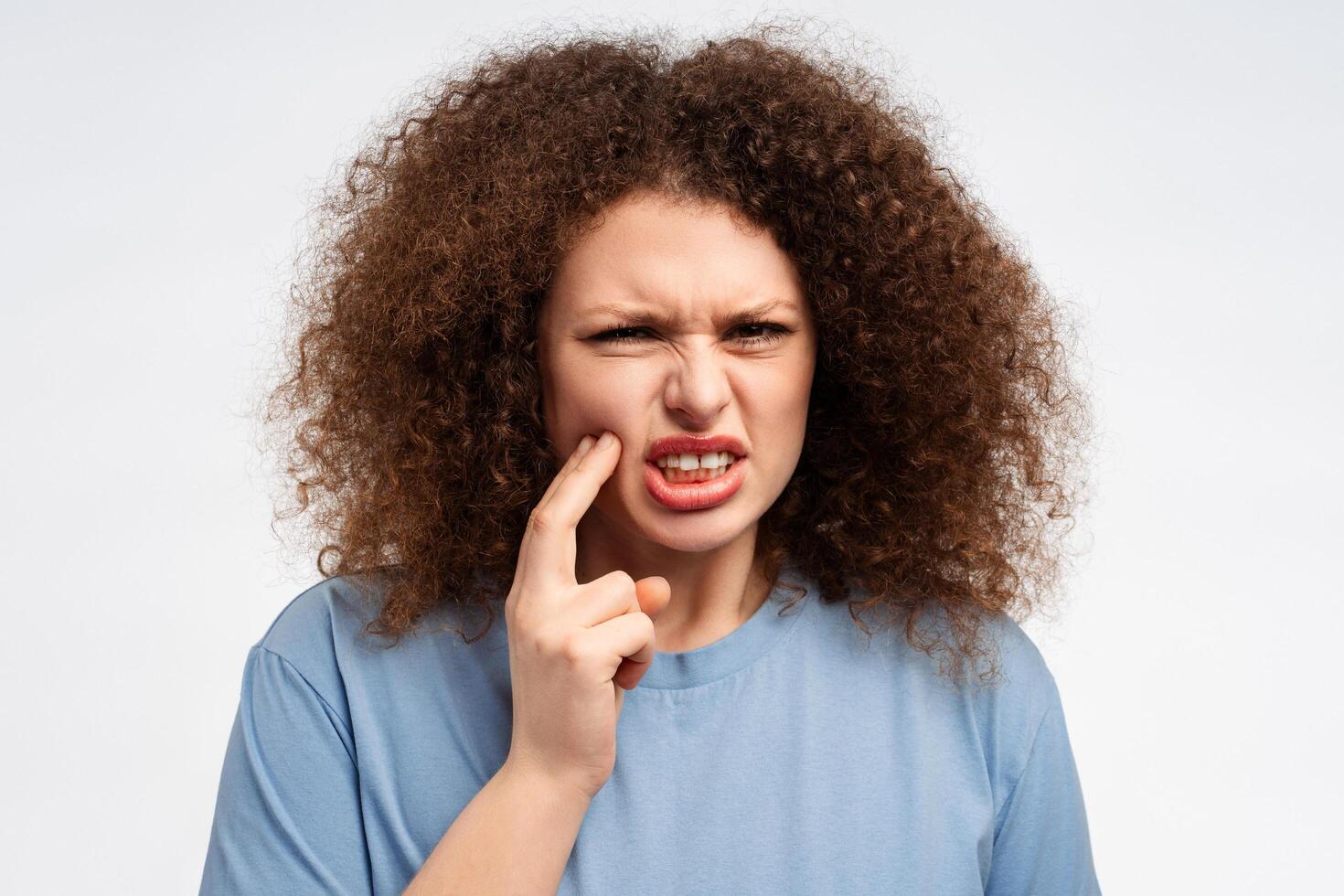 Portrait of upset young woman with curly hair touching face, toothache, looking at camera photo