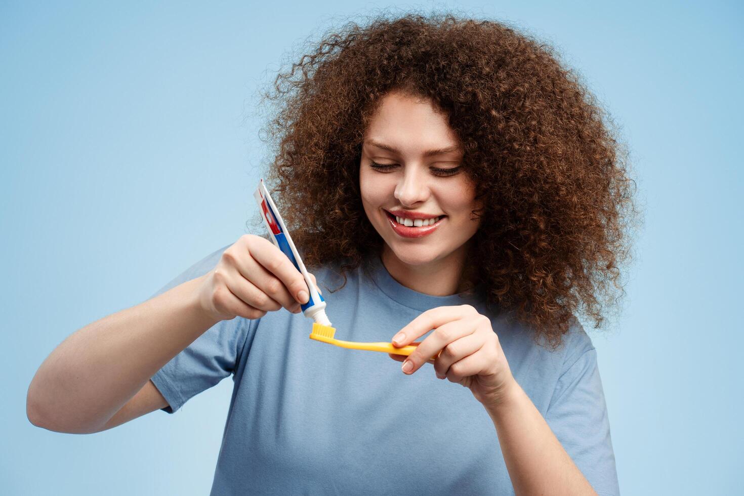 Beautiful, smiling young woman with curly hair holding toothbrush and toothpaste, brushing her teeth photo