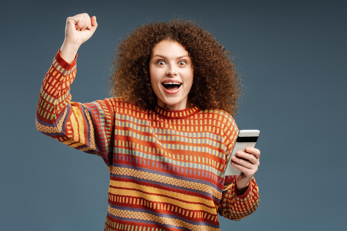 Attractive, smiling, curly woman wearing casual sweater holding mobile phone using mobile app photo