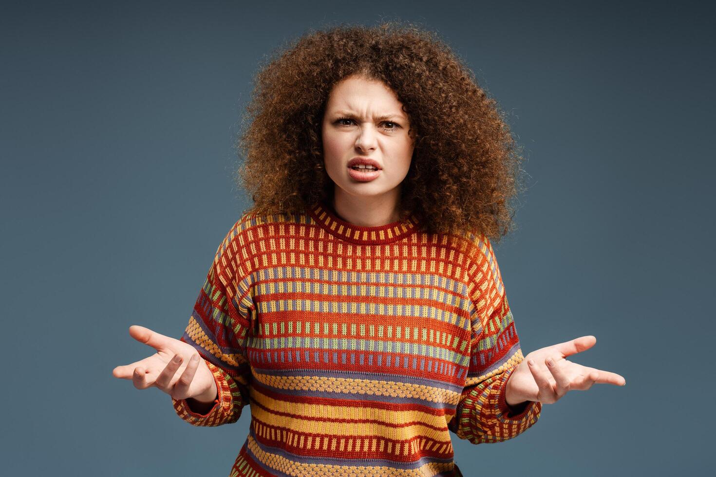 Young upset woman with curly hair wearing casual cheerful sweater looking at camera, gesturing photo