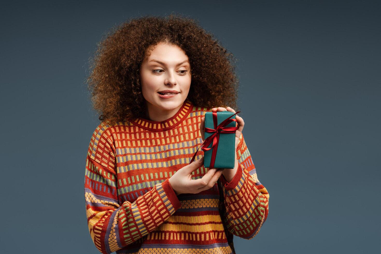 Excited beautiful woman with curly hair holding gift box for birthday photo