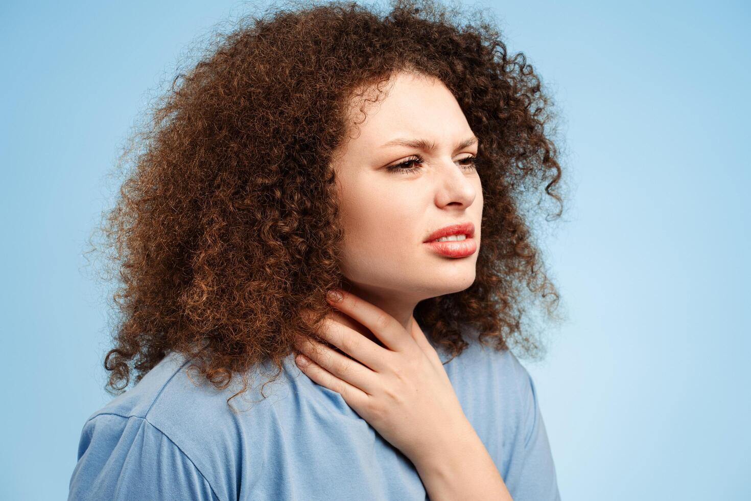 Upset sick young woman with curly hair having sore throat, cold, fever, looking away photo