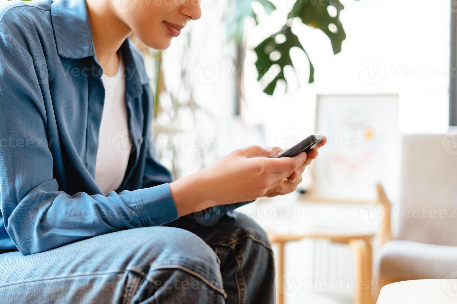 Smiling young woman holding mobile phone, using smartphone, watching , on comfortable sofa photo