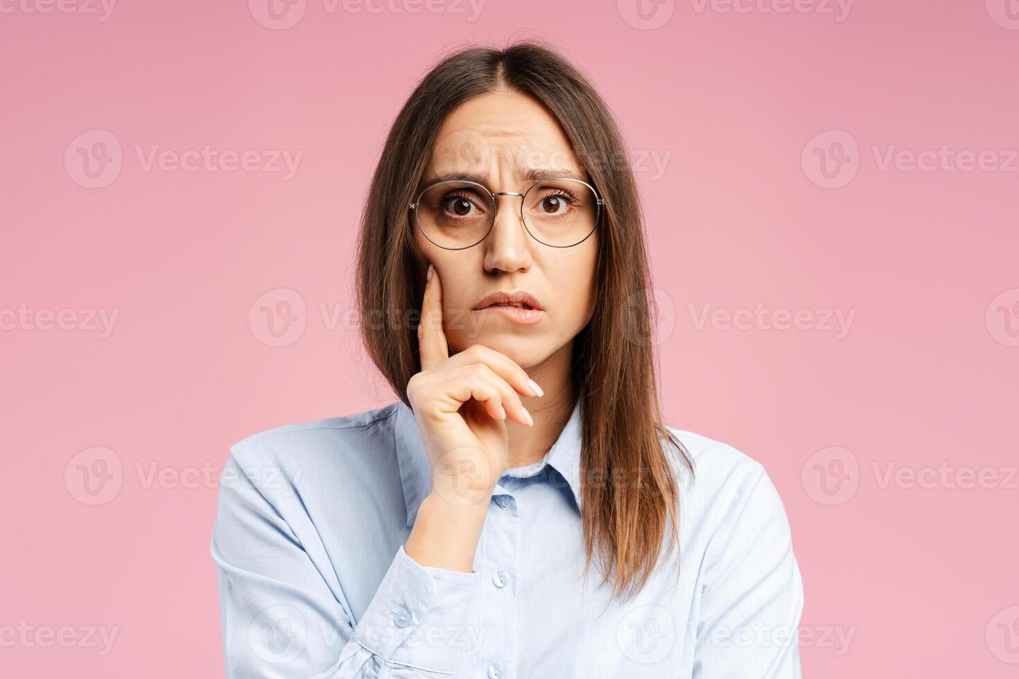 Pensive woman with glasses thinking, looking at camera, having confused facial expression photo
