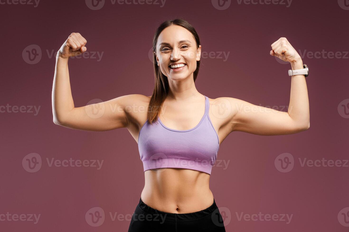 Happy Caucasian young woman showing biceps on her hands posing in studio, isolated photo