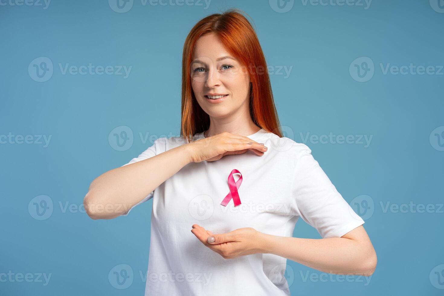 Woman showing pink ribbon attached to white t-shirt on blue background looking at camera photo