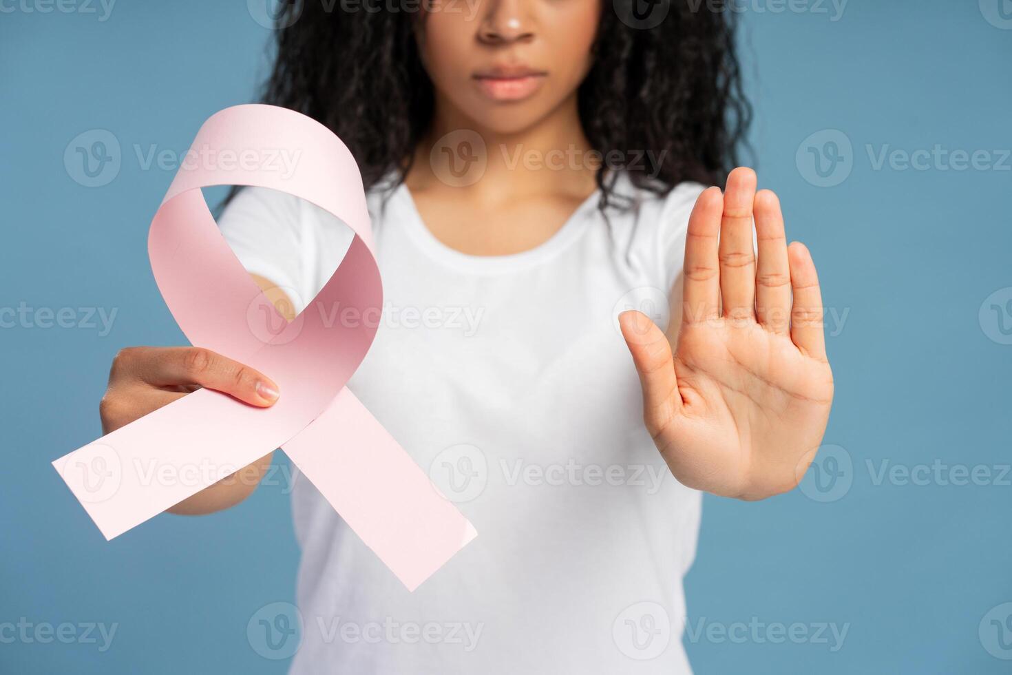 Woman showing pink ribbon and making stop gesture against blue background closeup selective focus photo