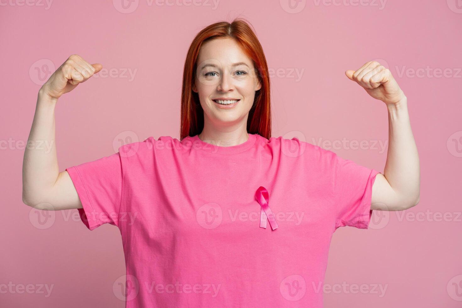 Smiling woman wearing pink t shirt with pink ribbon showing biceps isolated on pink background photo