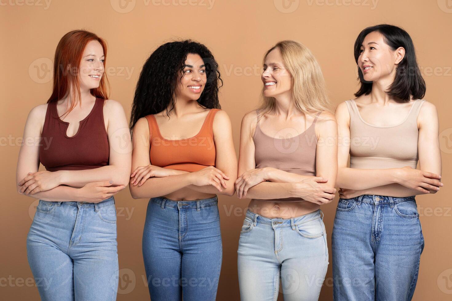Four confident women standing together with arms crossed smiling and looking at each other photo
