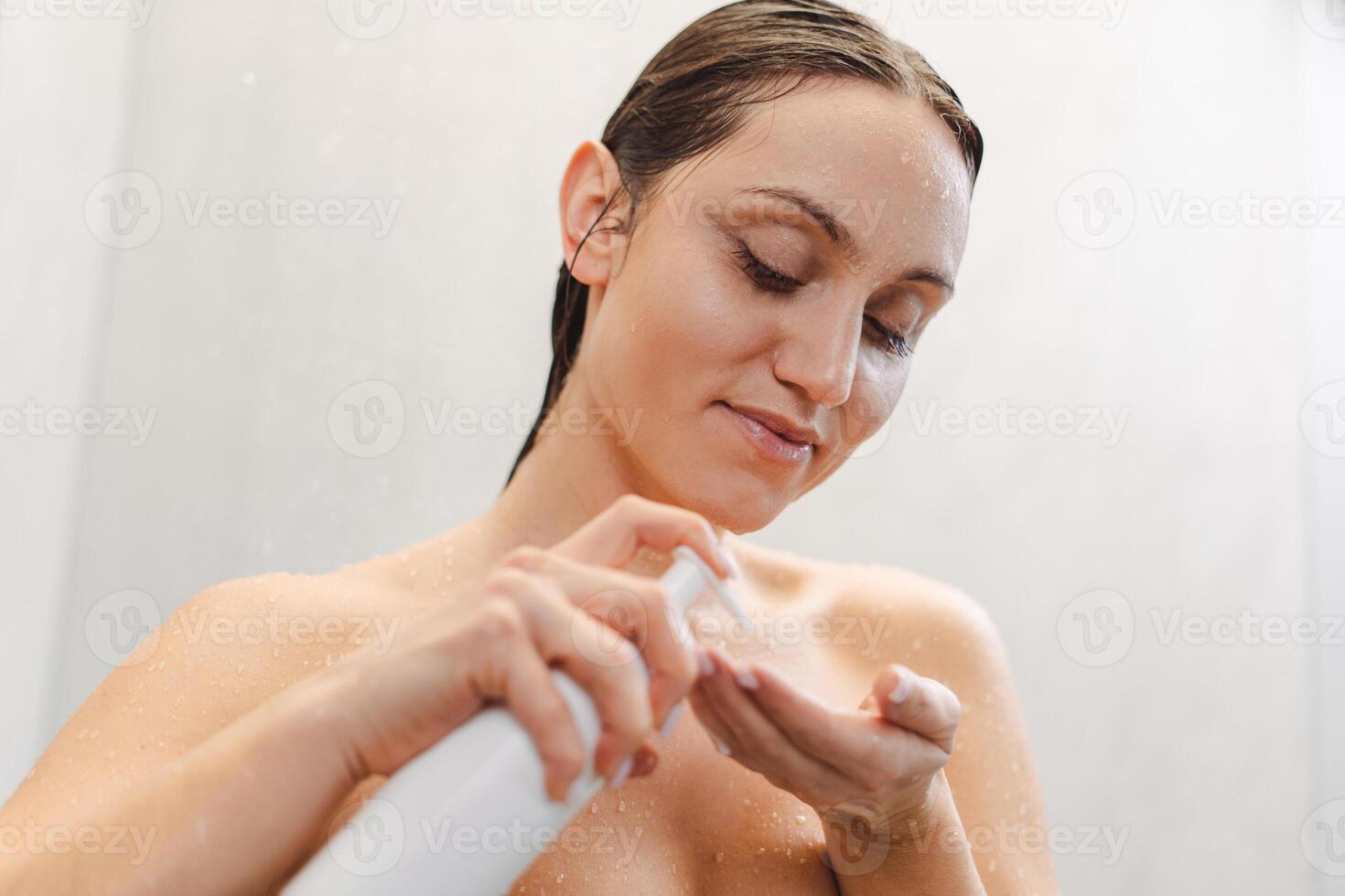 Relaxed calm woman pouring gel at her hands while taking hot shower photo