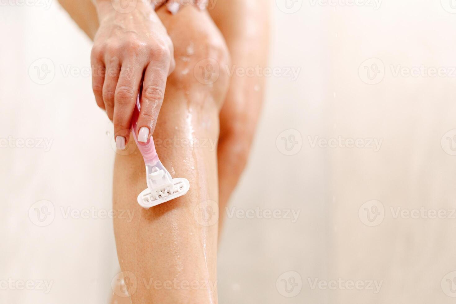 Woman shaving legs using safety razor in bathtub, enjoying depilation routine taking bath photo