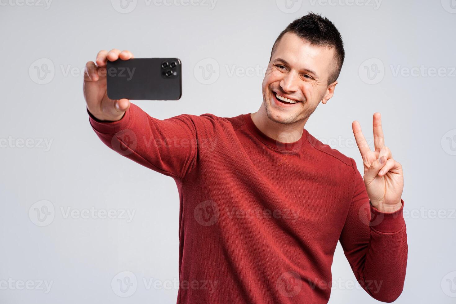 Smiling attractive man taking selfie on phone, hand gesture, making peace gesture photo