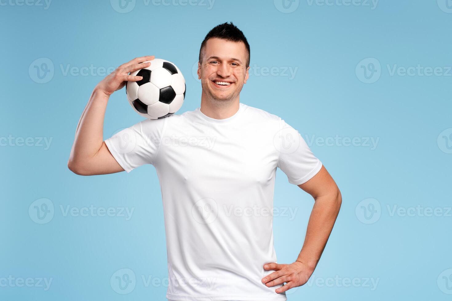 Handsome sportsman smiling and holding soccer ball on blue background photo
