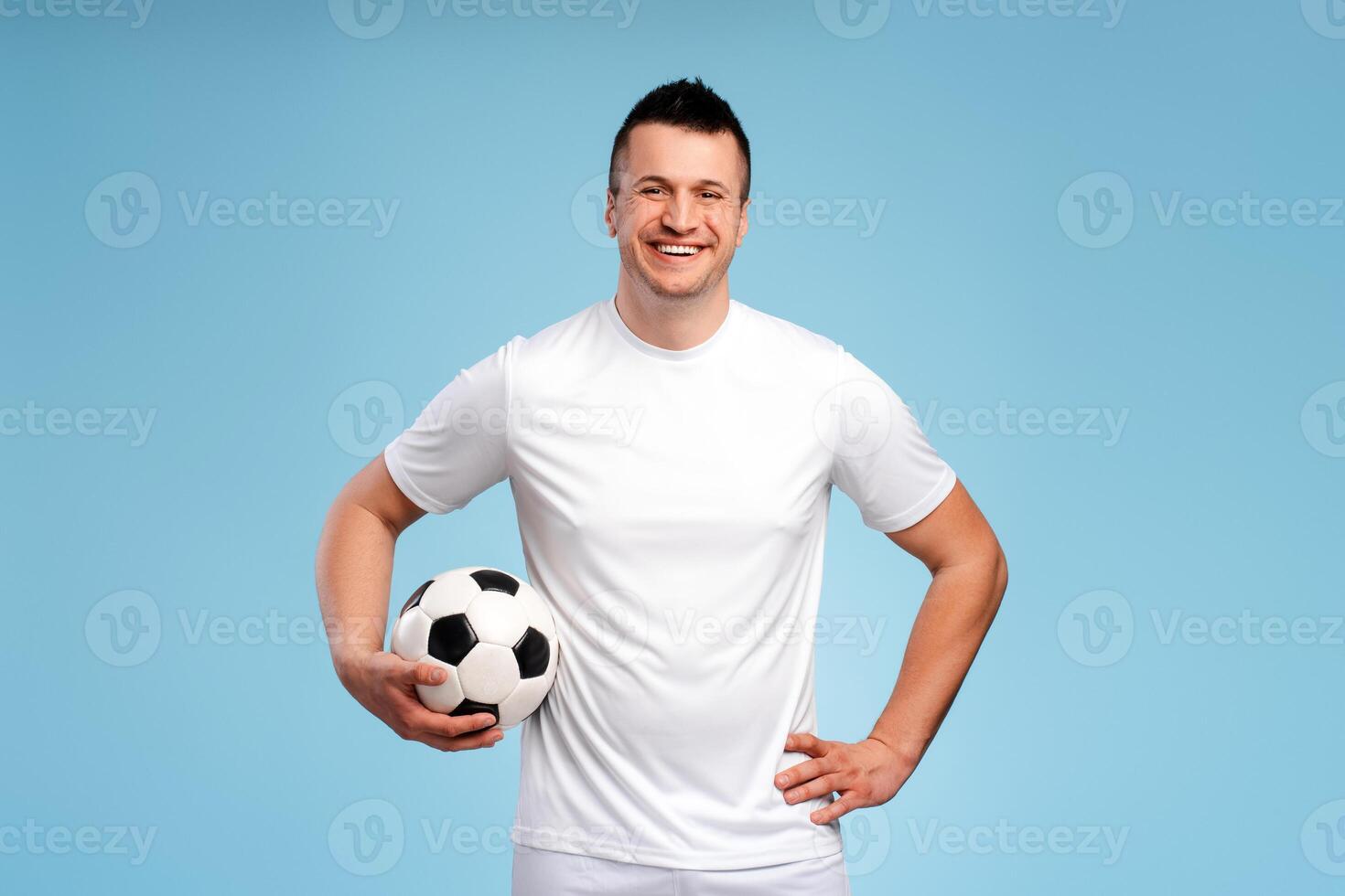 Happy soccer player holding a ball smiling at blue background photo
