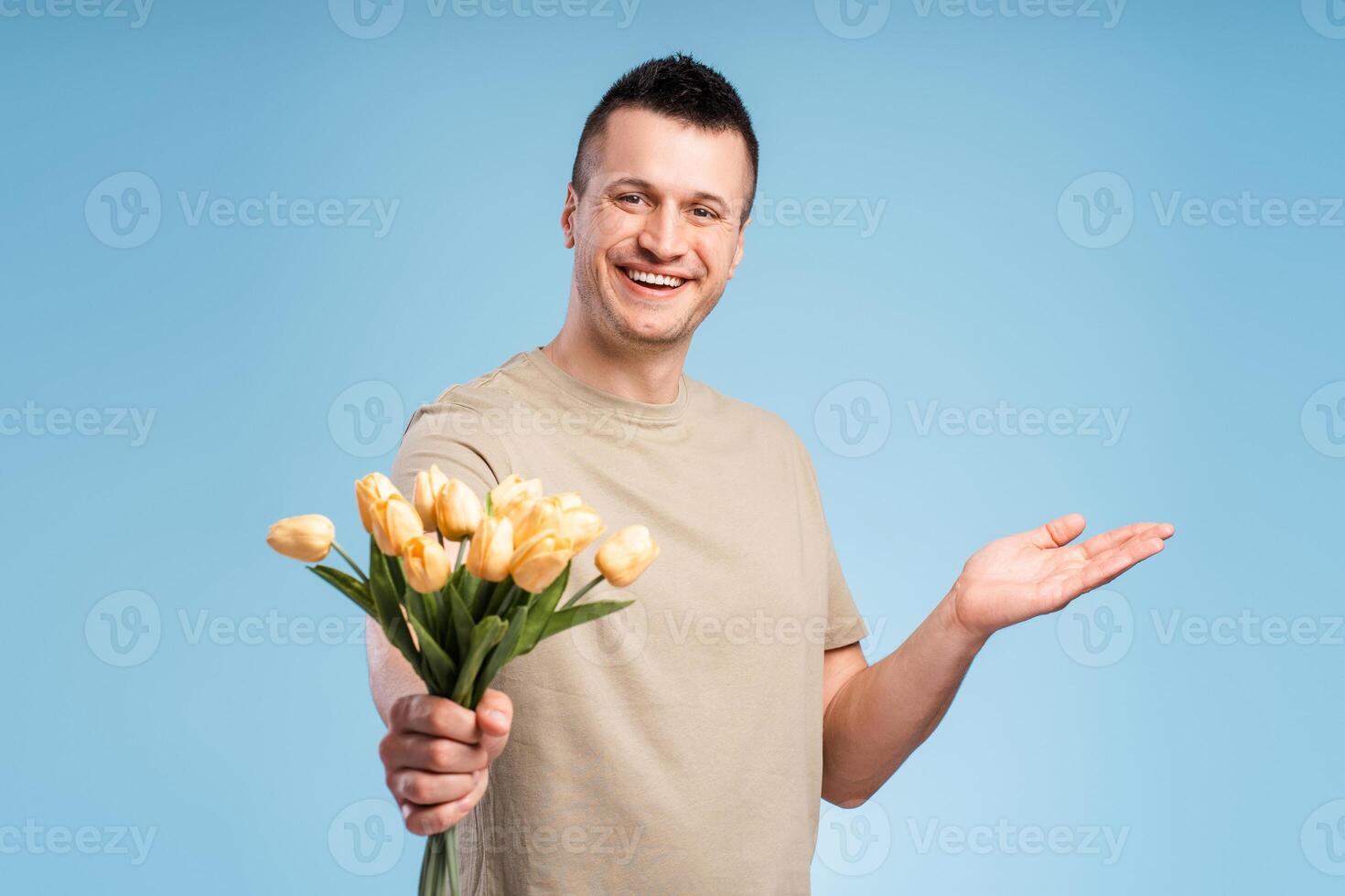 Handsome, smiling man looking at camera holding bouquet of flowers and pointing to copy space photo