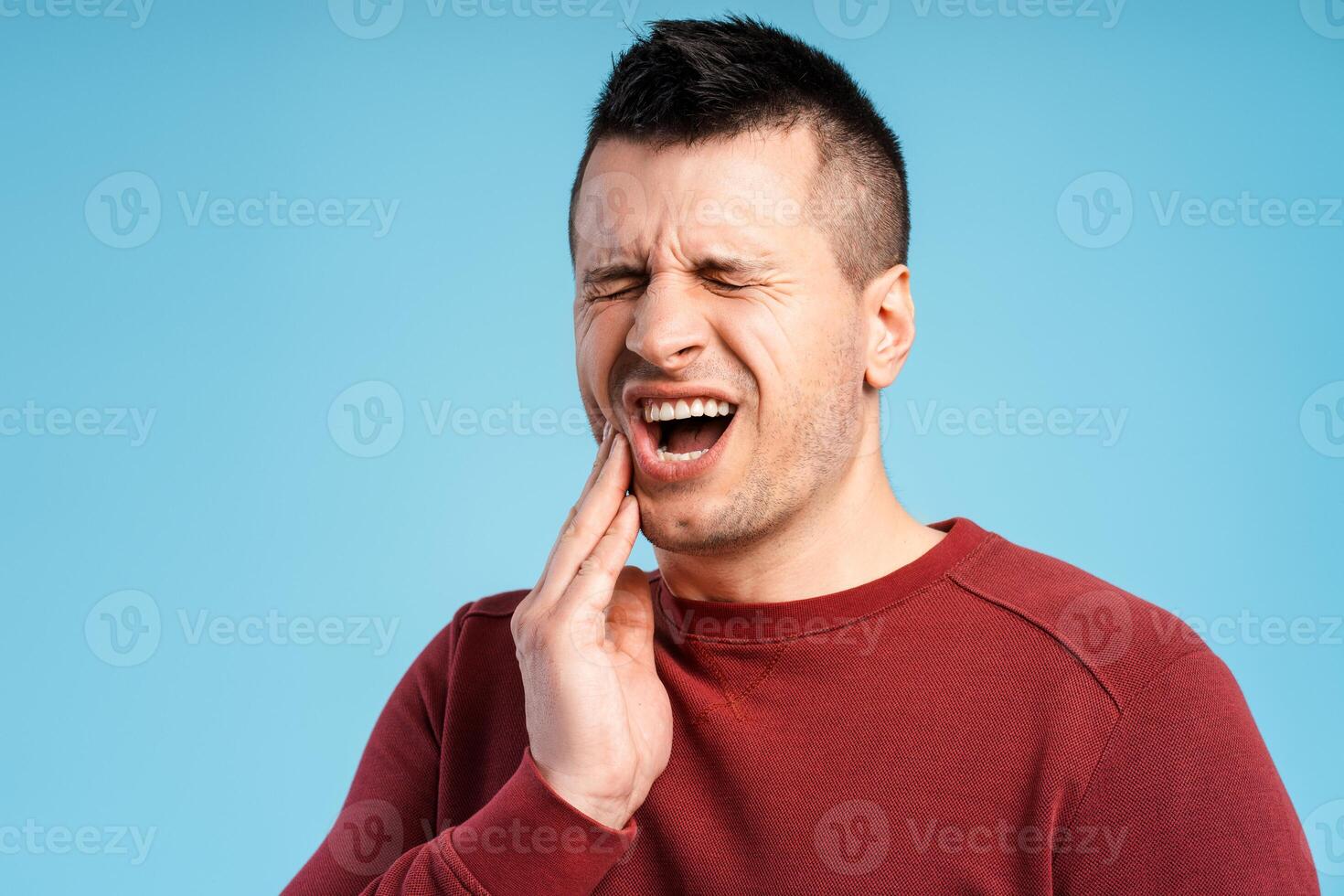 Middle aged man with closed eyes having teeth pain, standing on blue background photo