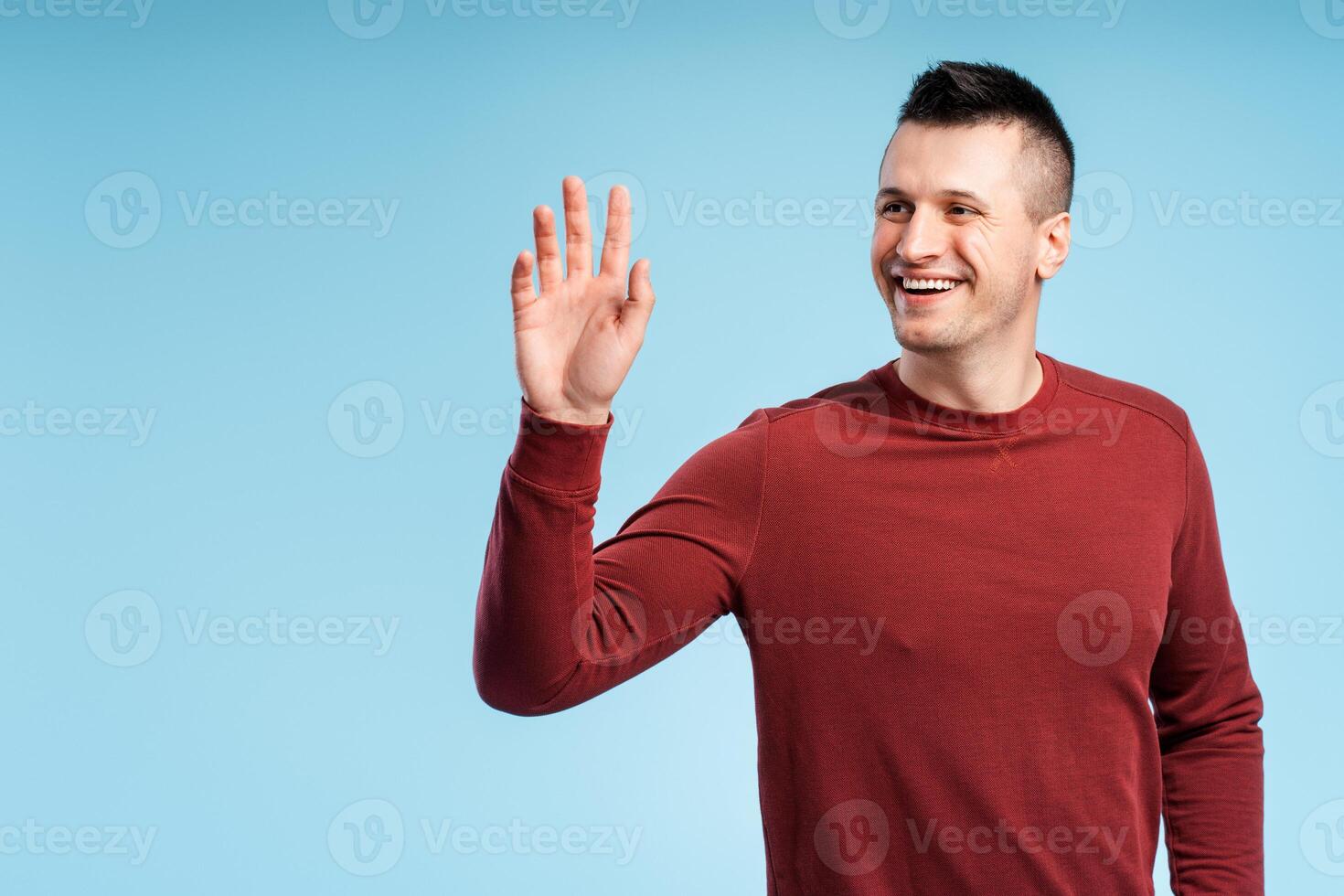 Middle aged man in red sweatshirt waving and saying hello, goodbye gesture, friendly welcome gesture photo