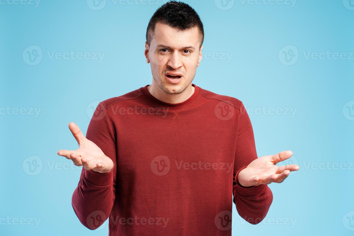 Dissatisfied, upset man in red sweater on blue background throws up his hands in frustration photo