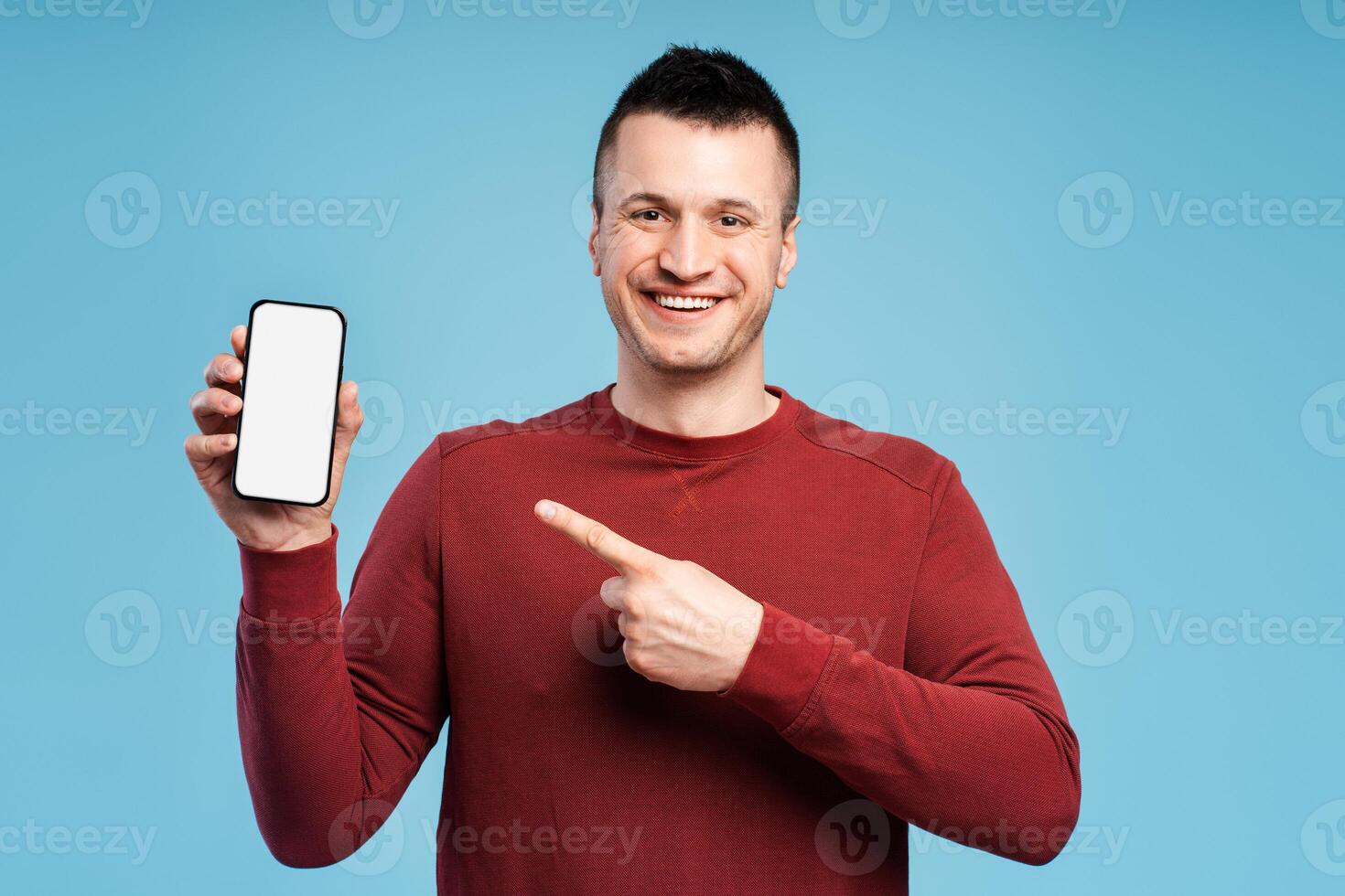 Smiling man pointing his finger at screen of his mobile phone phone isolated on blue background photo