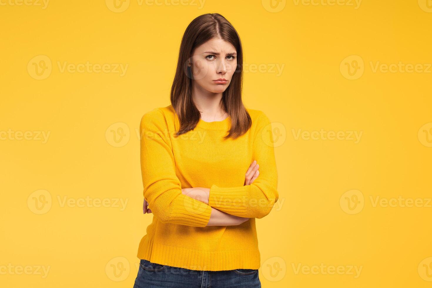 Offended, beautiful woman with arms crossed looking at camera standing isolated on yellow background photo