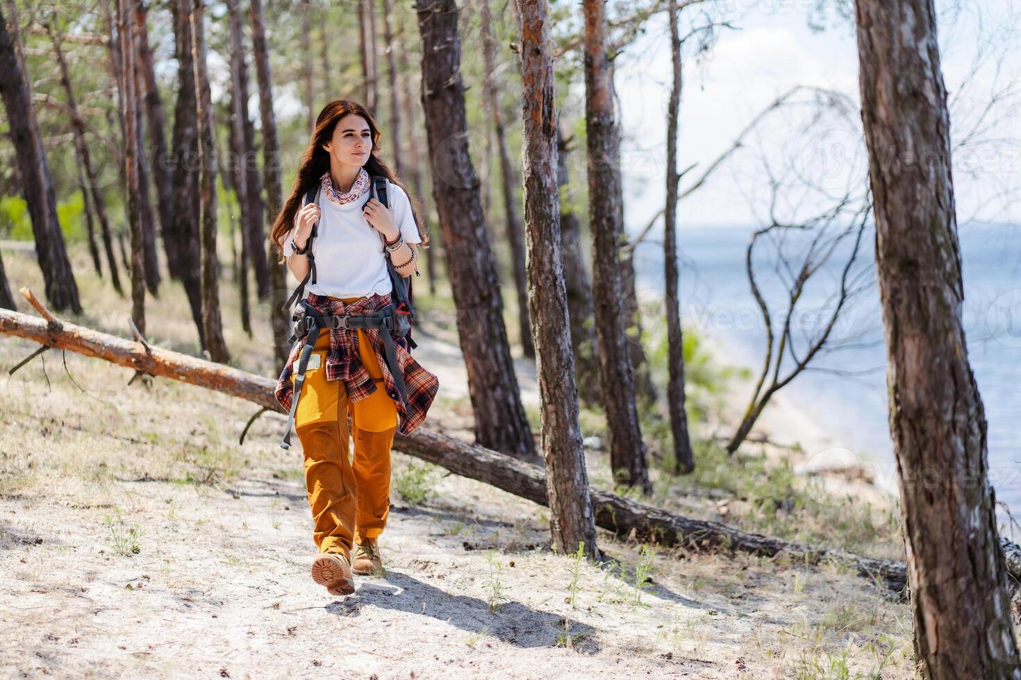 Young woman with backpack looking at the treetops in a pine forest while walking alone photo