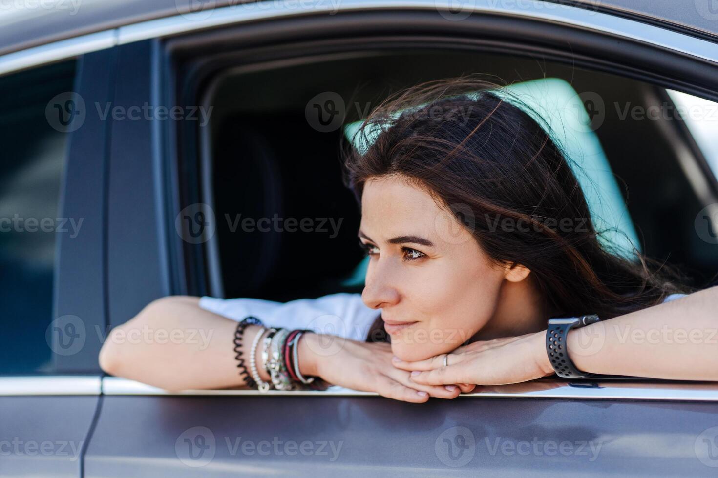 Dreamy smiling woman relaxing in car and looking window in summer photo