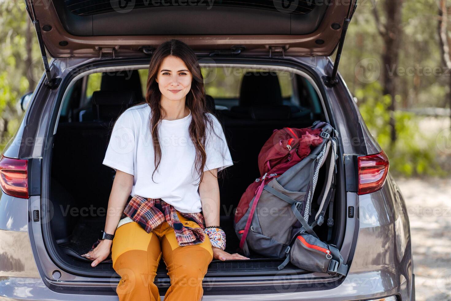 Beautiful, young woman sitting and relaxing on her car trunk, ready to go hiking photo